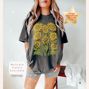May include: A dark grey t-shirt with a vintage-style graphic of yellow sunflowers on a green stem. The text "Multiple Colors Available" and "PEPPER" are printed on the bottom left corner of the shirt.