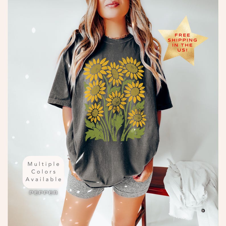 May include: A dark grey t-shirt with a vintage-style graphic of yellow sunflowers on a green stem. The text "Multiple Colors Available" and "PEPPER" are printed on the bottom left corner of the shirt.