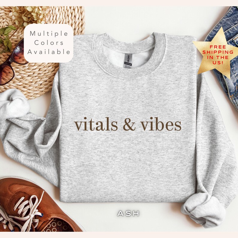 May include: A gray sweatshirt with the text "vitals & vibes" printed in brown on the front. The sweatshirt is available in multiple colors.