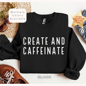 Puede incluir: Sudadera negra con el texto "CREATE AND CAFFEINE" en letras blancas. La sudadera está disponible en varios colores.