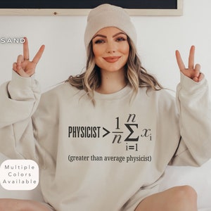 Könnte beinhalten: Ein beiger Pullover mit einem schwarzen Grafikdruck, der "PHYSICIST> 1/n Σn=1 xi (greater than average physicist)" lautet.