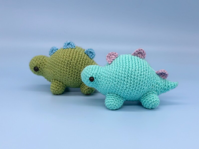 May include: Two crocheted dinosaur toys, one green and one blue, with black eyes.