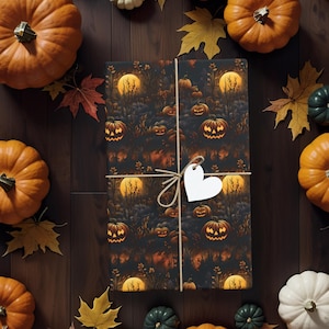 May include: A rectangular gift wrapped in dark paper featuring a repeating pattern of glowing jack-o'-lanterns and full moons. The package is tied with thin twine and includes a blank white heart-shaped gift tag attached to the centre.