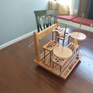 May include: A wooden craft organizer with multiple levels and compartments. It features various sized holes, platforms, and holders for tools and supplies. The organizer includes two circular platforms with metal rods, and a tray with small items.