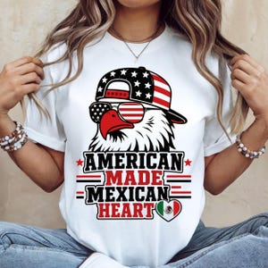 Op de afbeelding: Een wit t-shirt met een afbeelding van een Amerikaanse zeearend die een baseballpet en zonnebril met Amerikaanse vlagpatronen draagt. Onder de adelaar staat de tekst AMERICAN MADE MEXICAN HEART met een hartje in de Mexicaanse vlagkleuren.