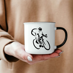 Puede incluir: Taza de cer&aacute;mica blanca con un contorno negro y una silueta negra de un ciclista montando una bicicleta.