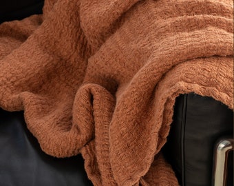 May include: A brown waffle weave throw blanket draped over a black leather armchair.