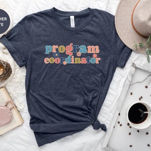 May include: A heather slate blue t-shirt with the text "program coordinator" in colorful letters with flowers.