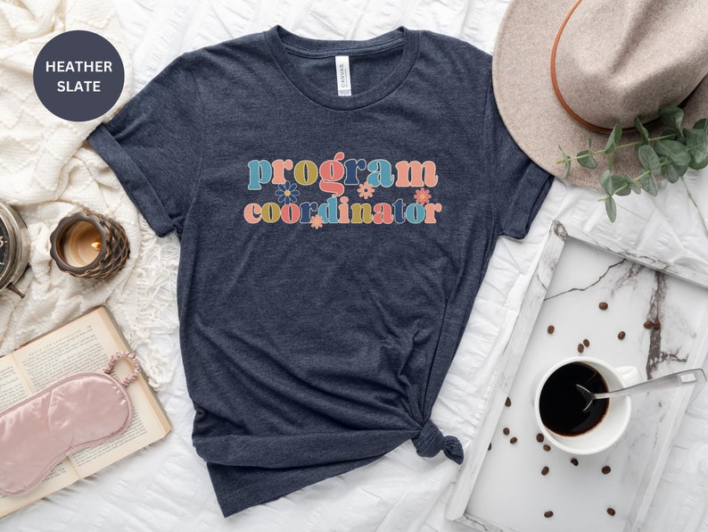 May include: A heather slate blue t-shirt with the text "program coordinator" in colorful letters with flowers.