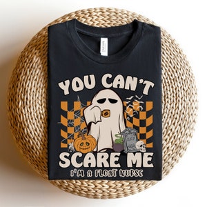 May include: Black t-shirt with a Halloween-themed design featuring a ghost holding a cup of coffee, a pumpkin, a cauldron, and a tombstone with the text "RIP Sleep". The text on the shirt reads "You Can't Scare Me I'm a Float Nurse".