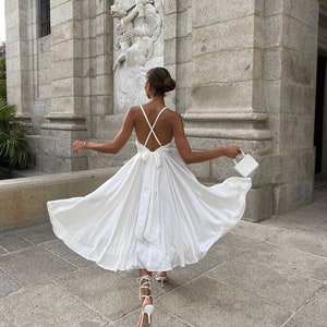 Atemberaubendes weißes Seidenkleid mit offenem Rücken. Kleid mit Tellerrock aus Satin mit Trägern. Brautjungfernkleid mit V-Ausschnitt in Midi-Länge. Rückenfreies Eventkleid. White