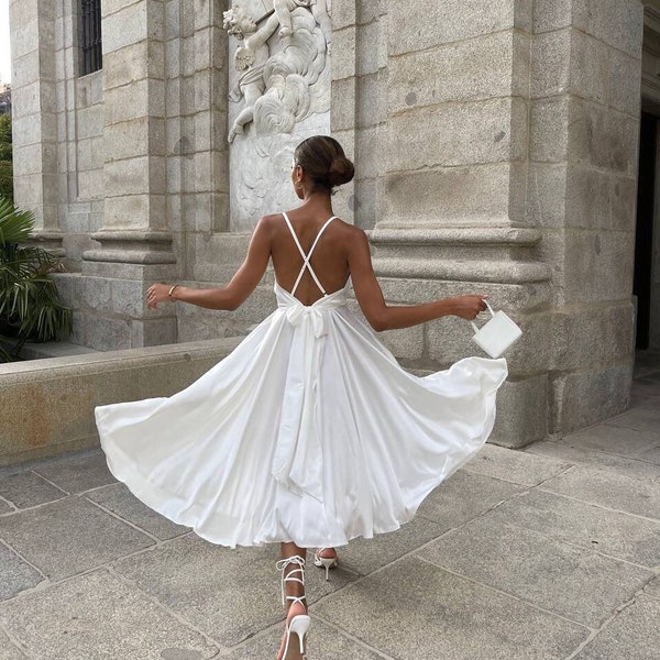 Atemberaubendes weißes Seidenkleid mit offenem Rücken. Kleid mit Tellerrock aus Satin mit Trägern. Brautjungfernkleid mit V-Ausschnitt in Midi-Länge. Rückenfreies Eventkleid.
