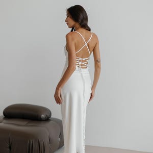 Abito sottoveste bianco in seta senza schienale per occasioni speciali. Abito in raso a trapezio con scollo a cappuccio e schiena scoperta con lacci. Abito in seta con spalline in color latte.