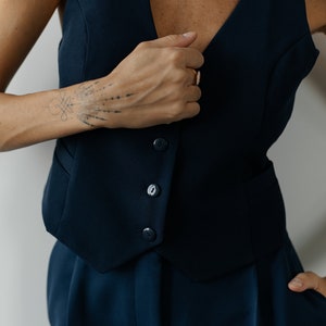 May include: A navy blue sleeveless vest with four buttons and a matching pair of pants. The vest has a deep V-neckline.
