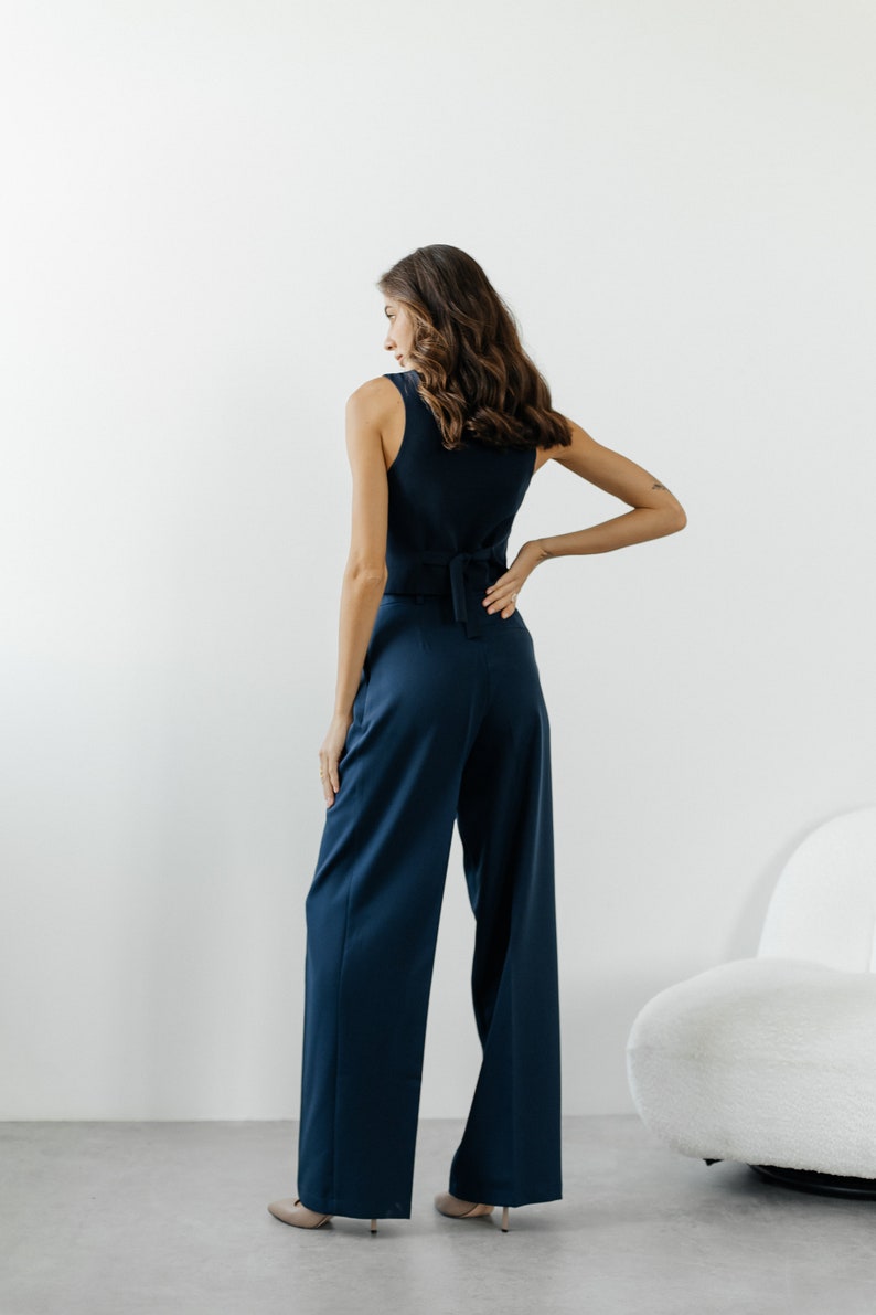 May include: A woman wearing a dark blue sleeveless top with a tie at the back and matching wide-leg pants.
