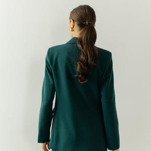 May include: A woman wearing a dark green blazer and matching pants. The blazer has a classic cut and a double-breasted closure.
