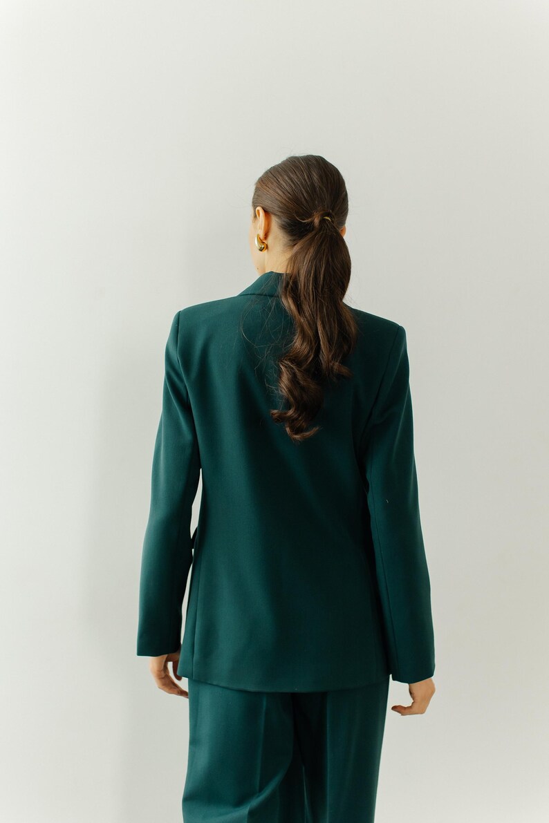 May include: A woman wearing a dark green blazer and matching pants. The blazer has a classic cut and a double-breasted closure.
