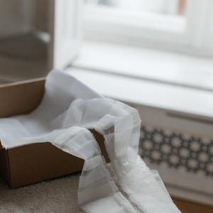 May include: A brown cardboard box with white tissue paper inside. The tissue paper is folded and draped over the edge of the box.