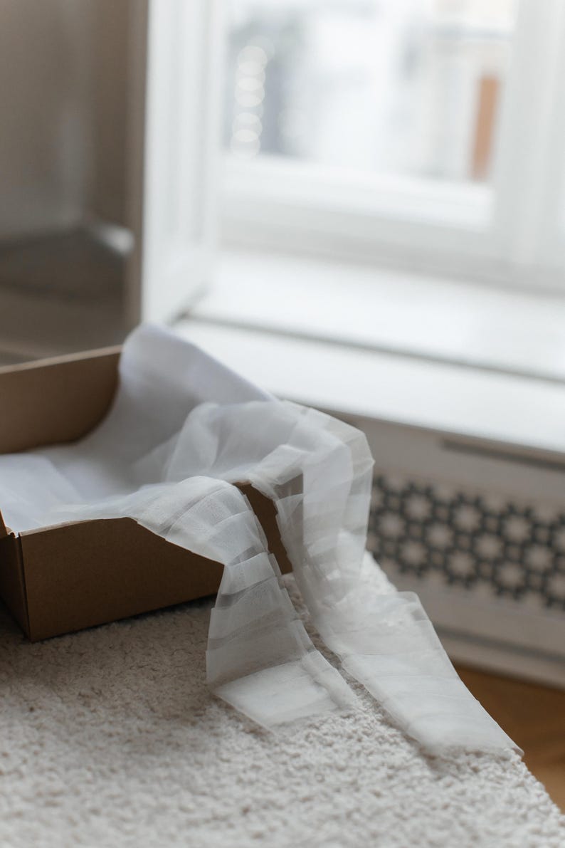 May include: A brown cardboard box with white tissue paper inside. The tissue paper is folded and draped over the edge of the box.