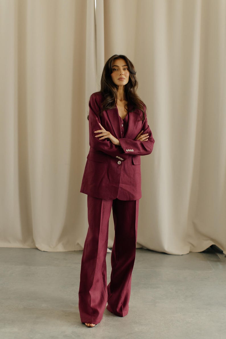 May include: A burgundy suit set, including a blazer and wide-leg pants. The blazer has a button closure and the pants have a flared design. The outfit is made of a smooth fabric and is suitable for formal or business attire.