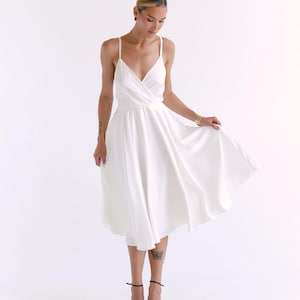 Peut inclure: Une robe blanche en portefeuille avec un d&eacute;collet&eacute; en V et une jupe fluide. La robe est faite d'un tissu l&eacute;ger et a une coupe ample.