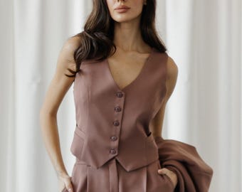 May include: A mauve-colored sleeveless vest with a V-neckline and five buttons. The vest is paired with matching wide-leg pants. The person is wearing a blazer draped over their shoulder.