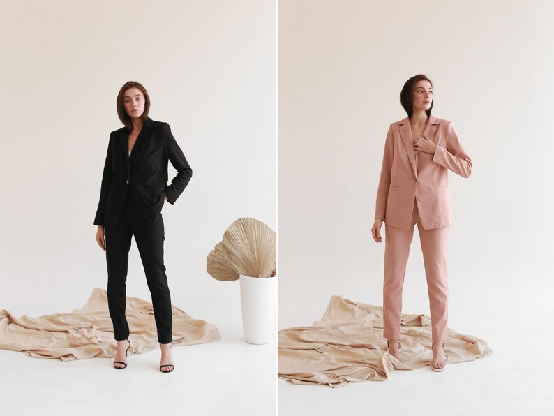 May include: Two women wearing matching suits, one in black and one in pink, standing on a beige surface. Both women are wearing heels and have their hair pulled back.
