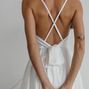 Peut inclure: Une robe blanche en satin avec un dos crois&eacute; et un n&oelig;ud papillon &agrave; la taille.
