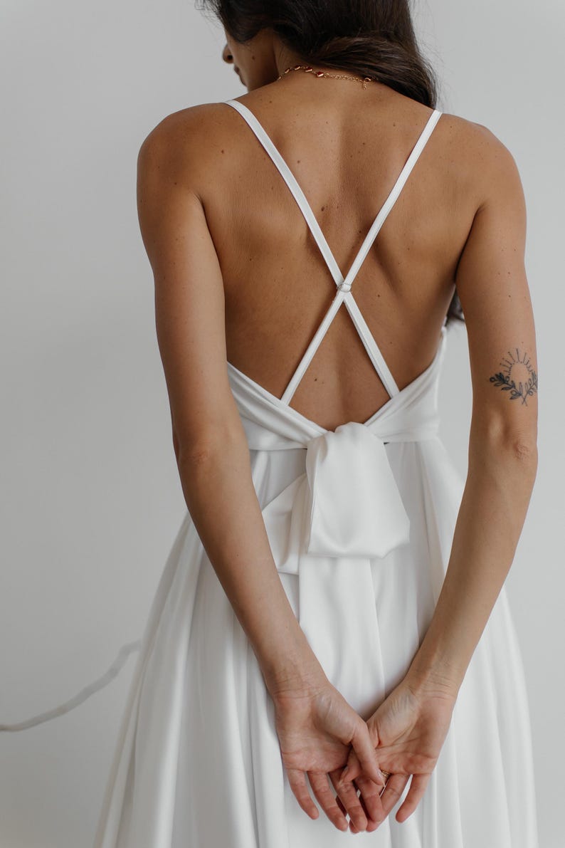 Peut inclure: Une robe blanche en satin avec un dos crois&eacute; et un n&oelig;ud papillon &agrave; la taille.