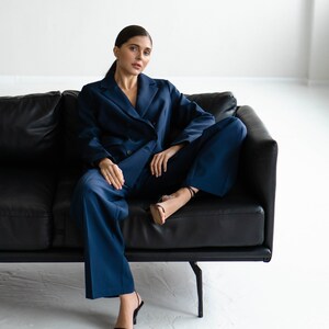 May include: A woman wearing a dark blue suit sits on a black leather sofa. She is wearing black heels and has her hair pulled back.