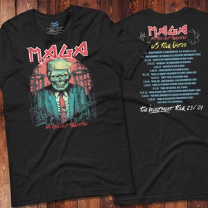 May include: A black t-shirt with a graphic of a skull wearing a suit and tie. The skull is wearing a red, white, and blue tie and has a chain around its neck. The text "MAGA" is printed in large, bold letters above the skull. The text "MY ASS GOT ARRESTED" is printed below the skull. The back of the shirt has a list of dates and locations for a "The Indictment Tour 23/24".