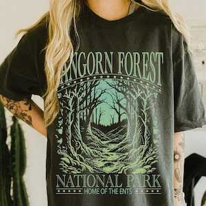 Könnte beinhalten: Dunkelgraues T-Shirt mit einem Wald-Motiv. Das Design zeigt den Text "Fangorn Forest National Park, Home of the Ents" in Grün. Die Grafik zeigt eine Waldszene mit Bäumen und einem Pfad.