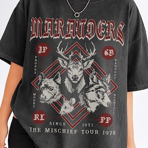 May include: Dark gray t-shirt with a graphic design featuring the word "Marauders" in a gothic font. The design includes a stag, a dog, and a wolf, with text that reads "The Mischief Tour 1978."