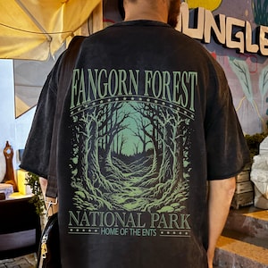 Op de afbeelding: Zwart oversized T-shirt met een groene afbeelding van een bos. De tekst "FANGORN FOREST" staat in een boog erboven, met "NATIONAL PARK" en "HOME OF THE ENTS" eronder.
