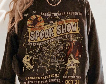 May include: Dark gray sweatshirt featuring a vintage-style Halloween design. The graphic reads "Midnight Spook Show" with illustrations of skeletons, a witch, and Frankenstein's monster. The text "One Night Only Oct 31" is also included.