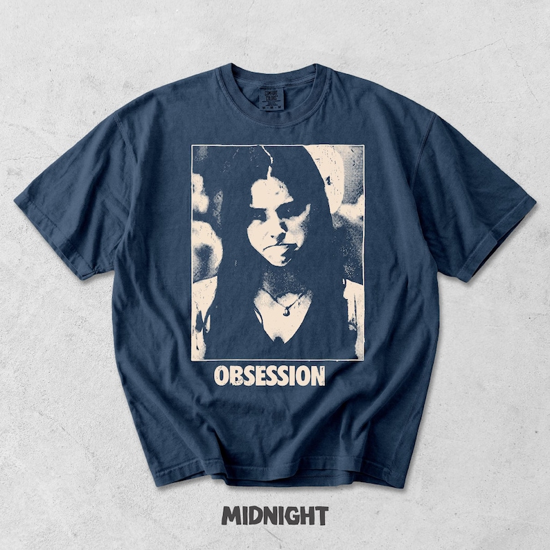 May include: A navy blue short-sleeve t-shirt featuring a rectangular graphic print of a person with long hair wearing a necklace. The word OBSESSION is printed in white capital letters below the image, and the word MIDNIGHT is below that.