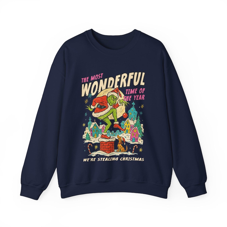 May include: Navy blue sweatshirt featuring a graphic of a green character in a Santa hat, carrying a sack. The graphic includes the text "THE MOST WONDERFUL TIME OF THE YEAR" and "WE'RE STEALING CHRISTMAS" with a winter village scene.