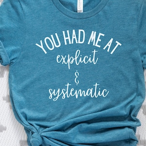 May include: A teal blue t-shirt with the text "You had me at explicit & systematic" printed in white.