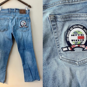 Peut inclure: Un jean en denim bleu clair avec un patch Tommy Jeans sur la poche arrière. Le patch est un cercle avec les mots "No Drugs, No Violence, Just Peace" et un logo Tommy Jeans.