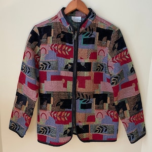 May include: A multi-coloured jacket with a geometric pattern and a zip closure. The jacket is made of a woven fabric and has a stand-up collar.