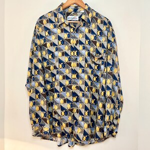 May include: A long-sleeved button-down shirt with a geometric pattern in shades of blue, yellow, and brown. The shirt has a collar and a pocket on the left side.
