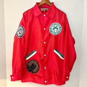 May include: Red nylon jacket with green and white trim. The jacket has several patches, including one that says "Masse League St. Jean Baptiste 72-73".