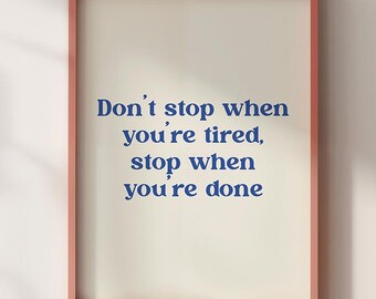 Puede incluir: Una impresión enmarcada con el texto "Don't stop when you're tired, stop when you're done" en fuente azul. La impresión tiene un fondo color crema y está encerrada en un marco color coral. La obra de arte se exhibe contra una pared neutra.