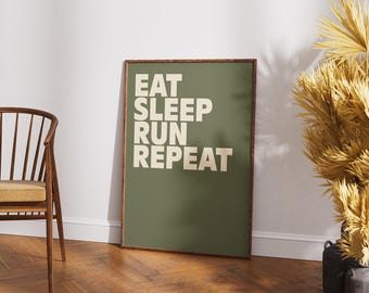 Pode incluir: Uma impressão emoldurada com as palavras "EAT SLEEP RUN REPEAT" em branco sobre um fundo verde. A moldura é marrom escuro. A impressão está encostada em uma parede branca.