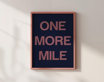 Pode incluir: Uma impressão emoldurada com as palavras "ONE MORE MILE" em letras cor-de-rosa sobre um fundo azul marinho. A moldura é de uma cor rosa a condizer. A impressão está pendurada numa parede bege clara.