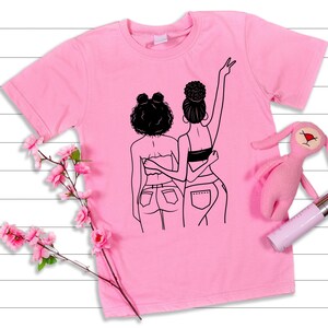 May include: Pink t-shirt with a black line drawing of two women with their arms around each other. The women are wearing jeans and have their hair pulled back.