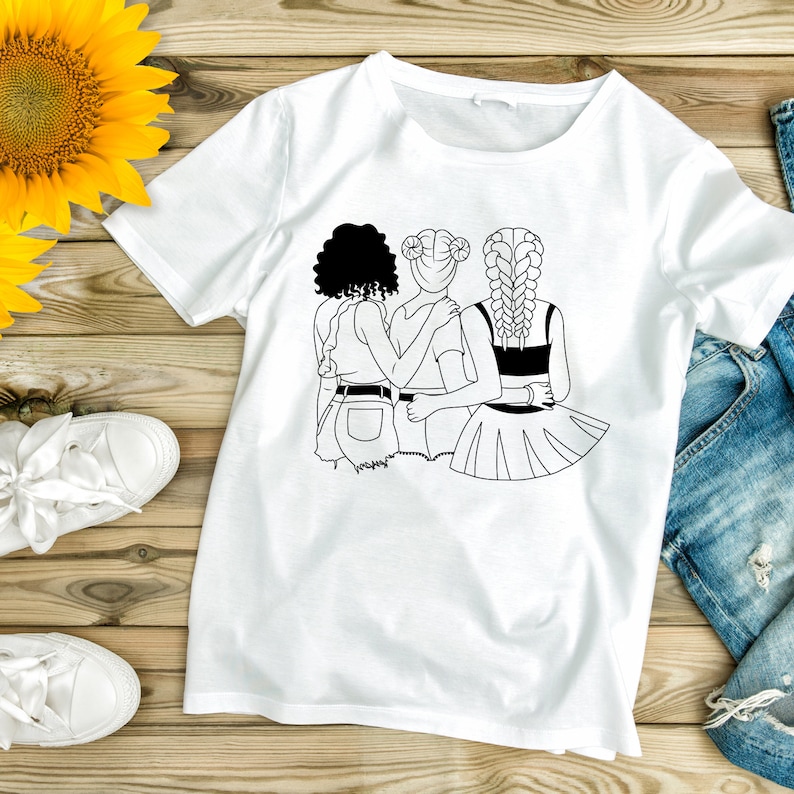 May include: A white t-shirt with a black line drawing of three women standing together. The women are wearing different hairstyles and outfits. The design is centered on the shirt.