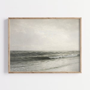 May include: A framed painting depicting a seascape with a cloudy sky and waves breaking on the shore. The painting is rendered in muted tones of grey and blue.