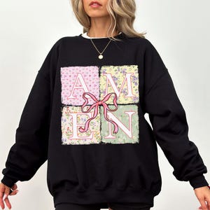 May include: Black sweatshirt with a floral print design that spells out the word "AMEN" in a patchwork style.