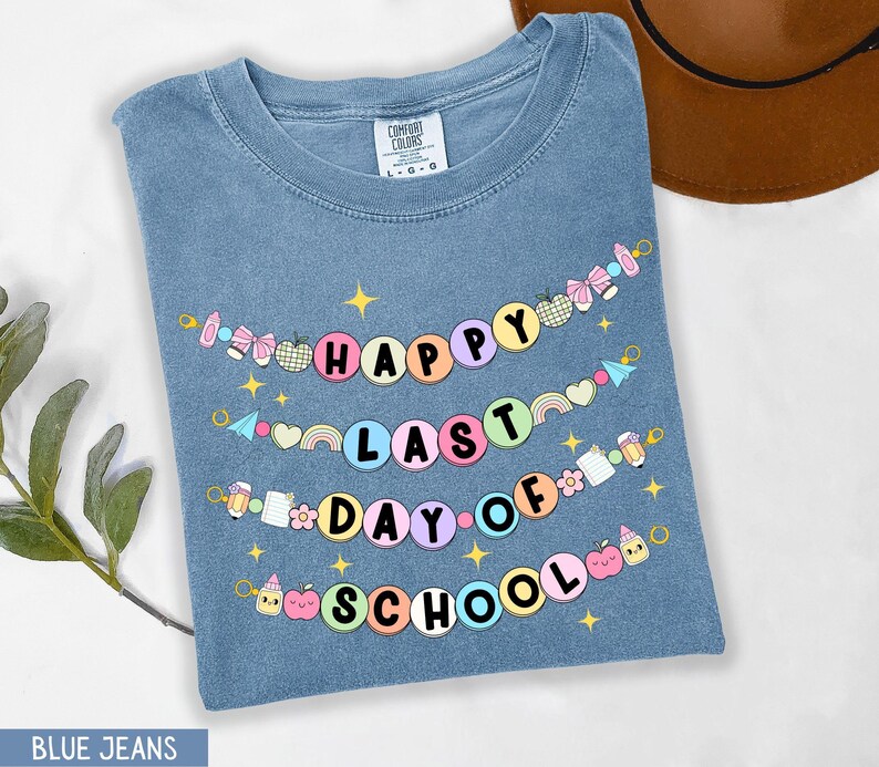 May include: A blue jean t-shirt with the text "Happy Last Day of School" in a colorful banner design. The banner is made of circles with different school-related icons and text.